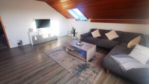 A modern living room with a sloped ceiling, a flat-screen TV, a grey sofa, and a wooden coffee table. - Vacation Apartment "Ländle" (Dauchingen)