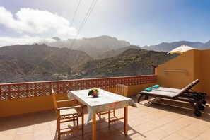 Un balcón con mesa, sillas y una tumbona con vistas a un paisaje montañoso.