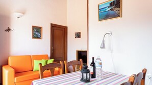 A room with a wooden door, a sofa, a table with a striped tablecloth, chairs, a small table with bottles, and a wall-mounted lamp.