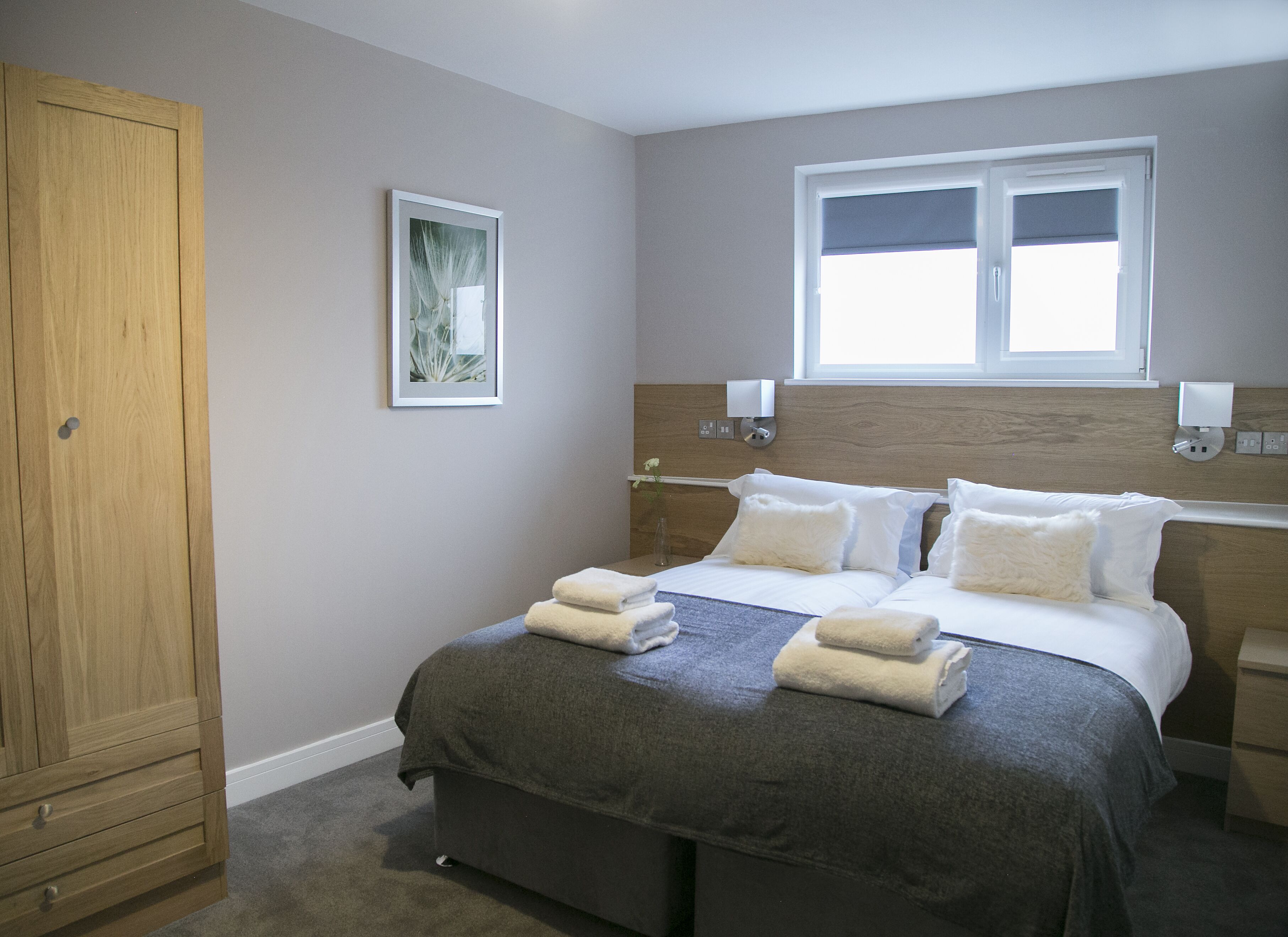 Une chambre d’hôtel avec un grand lit, une armoire, une fenêtre et un luminaire fixé au mur.