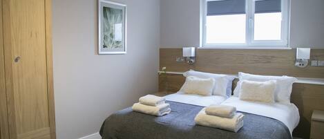 Une chambre d’hôtel avec un grand lit, une armoire, une fenêtre et un luminaire fixé au mur.