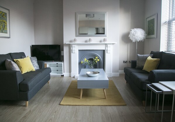 A modern living room with two sofas, a coffee table, a fireplace, and a television.