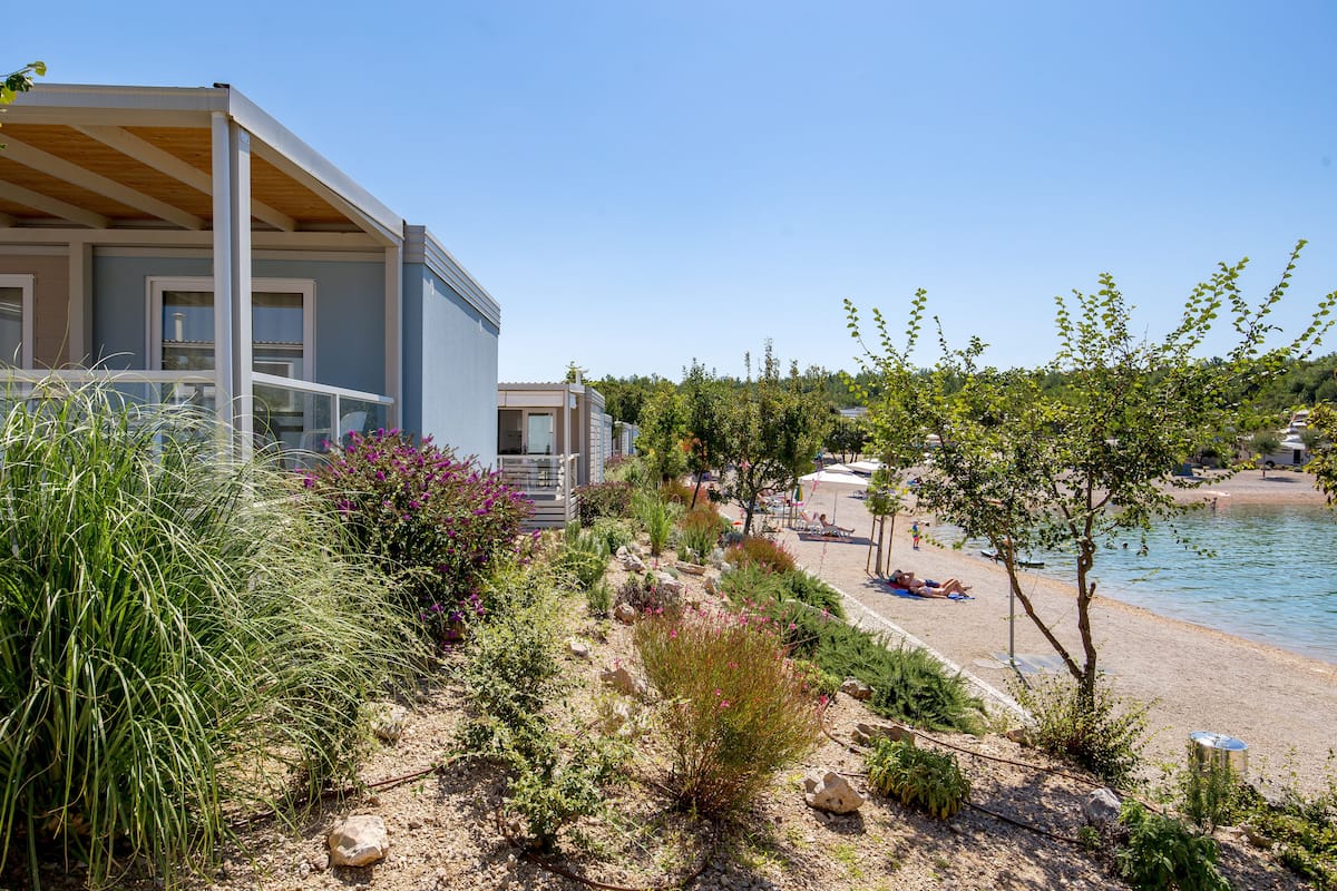 Un bâtiment moderne doté d’un espace extérieur couvert, d’un jardin aménagé et d’une plage où les gens se détendent.