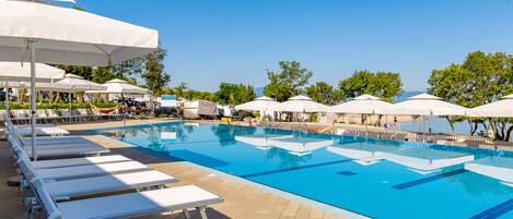 A swimming pool with sun loungers and umbrellas, surrounded by trees.