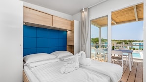 A modern hotel room with a large bed, a wooden headboard, and a view of a pool and outdoor seating area. - Mobile home Camping Omišalj (Omisalj)
