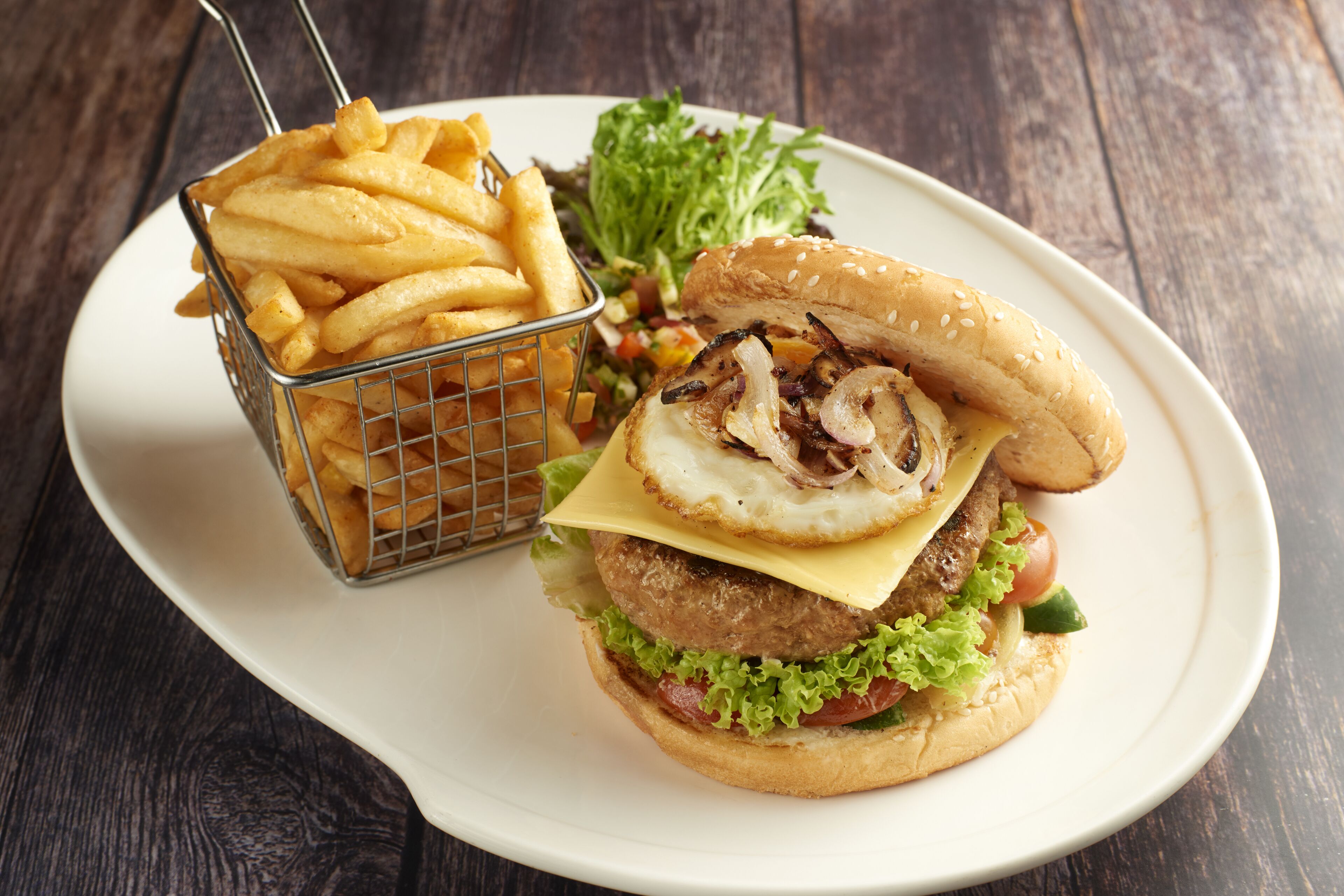 A burger with lettuce, tomato, and cheese, served with a side of fries on a white plate.