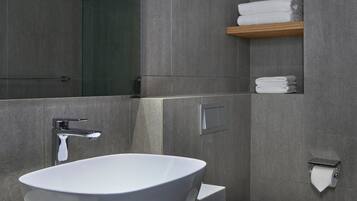 A modern bathroom with a freestanding bathtub, a towel rack with folded towels, and a toilet paper holder.