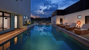 A modern indoor swimming pool with lounge chairs and a clear view of the sky. - Park Inn by Radisson Putrajaya (Bandar Baru Bangi)