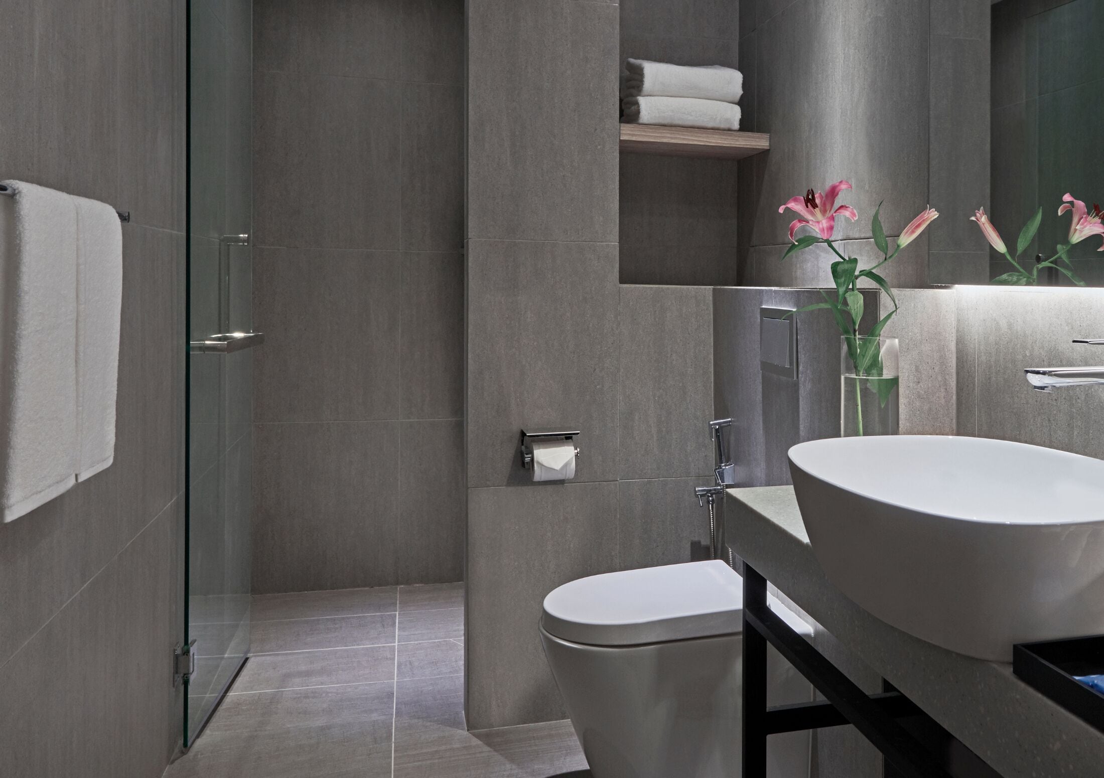 Un baño moderno con cabina de ducha de vidrio, inodoro, lavamanos con espejo y repisa con toallas.