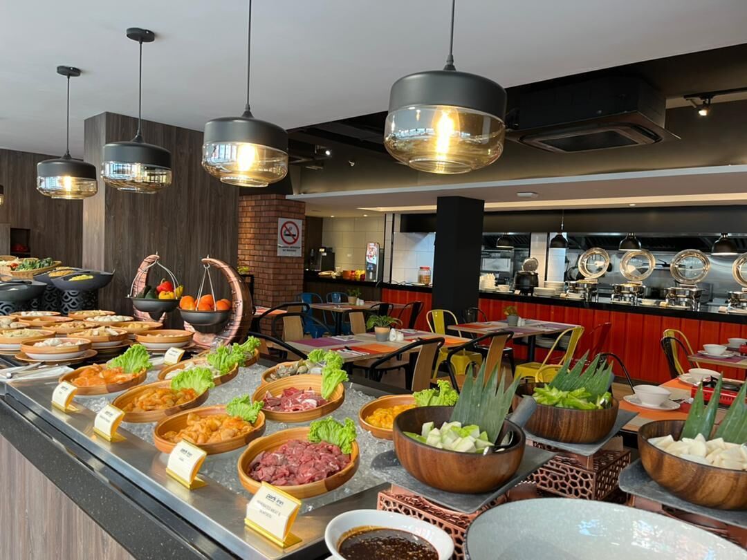 A buffet with various food options, including meats and vegetables, in a modern restaurant setting with hanging lights and a brick wall.