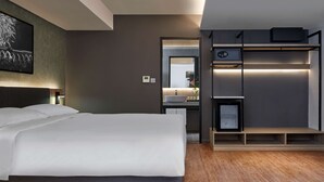 A modern hotel room with a large bed, a built-in desk with a mirror, a small kitchenette, and a wooden floor. - Park Inn by Radisson Putrajaya (Bandar Baru Bangi)