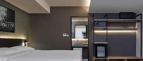 Une chambre d’hôtel moderne dotée d’un grand lit, d’un bureau intégré avec un miroir, d’une petite kitchenette et d’un plancher en bois.