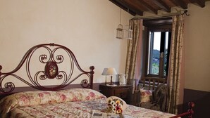 A bedroom with a wooden headboard, a floral bedspread, a nightstand with a lamp, and a window with curtains.