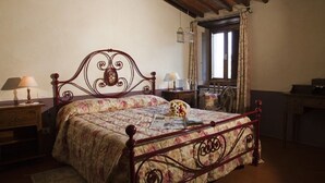 A bedroom with a wooden bed frame, floral bedding, a nightstand with a lamp, and a window with curtains.