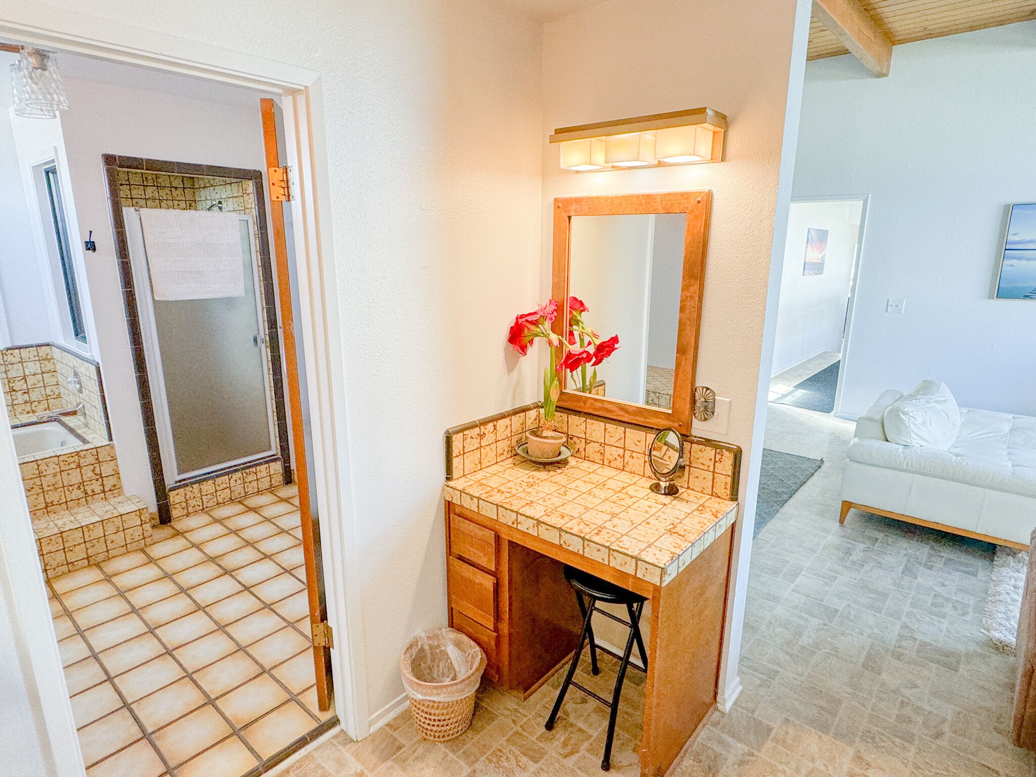A bathroom with a tiled floor, a sink with a mirror, a potted plant, and a towel hanging on the door.
