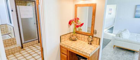 A bathroom with a tiled floor, a sink with a mirror, a potted plant, and a towel hanging on the door.