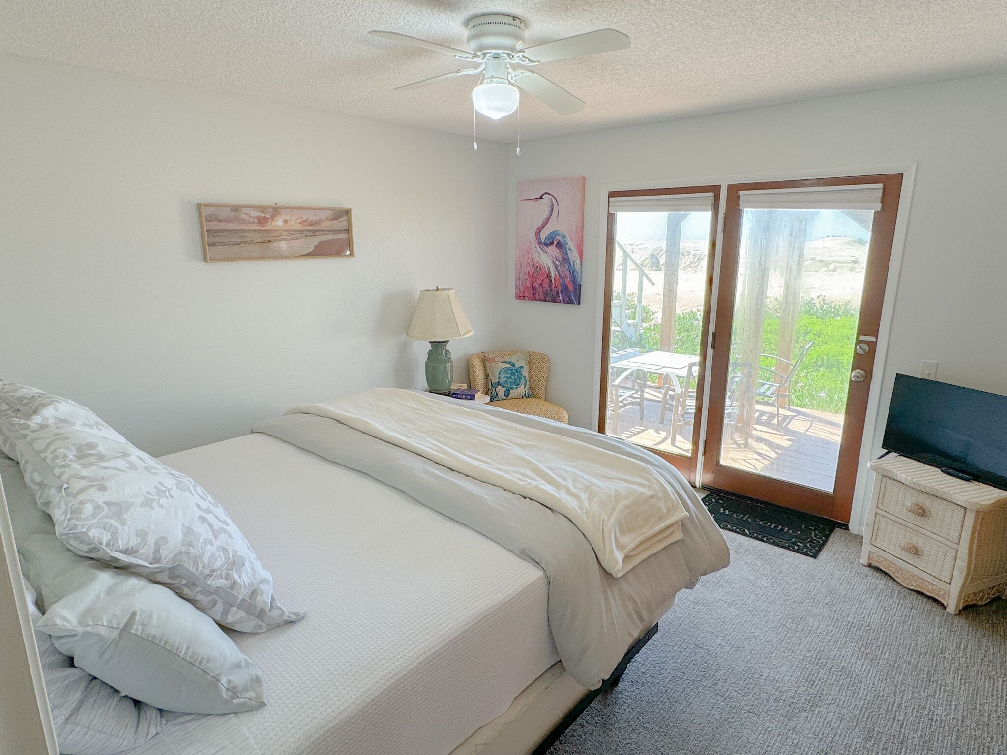 Una camera da letto con un letto, una ventola a soffitto, un quadro, una lampada e vista panoramica attraverso una porta in vetro.