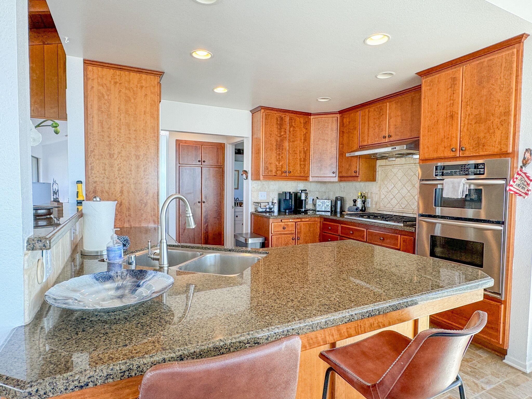 A modern kitchen with granite countertops, stainless steel appliances, wooden cabinets, and a large island with bar stools.