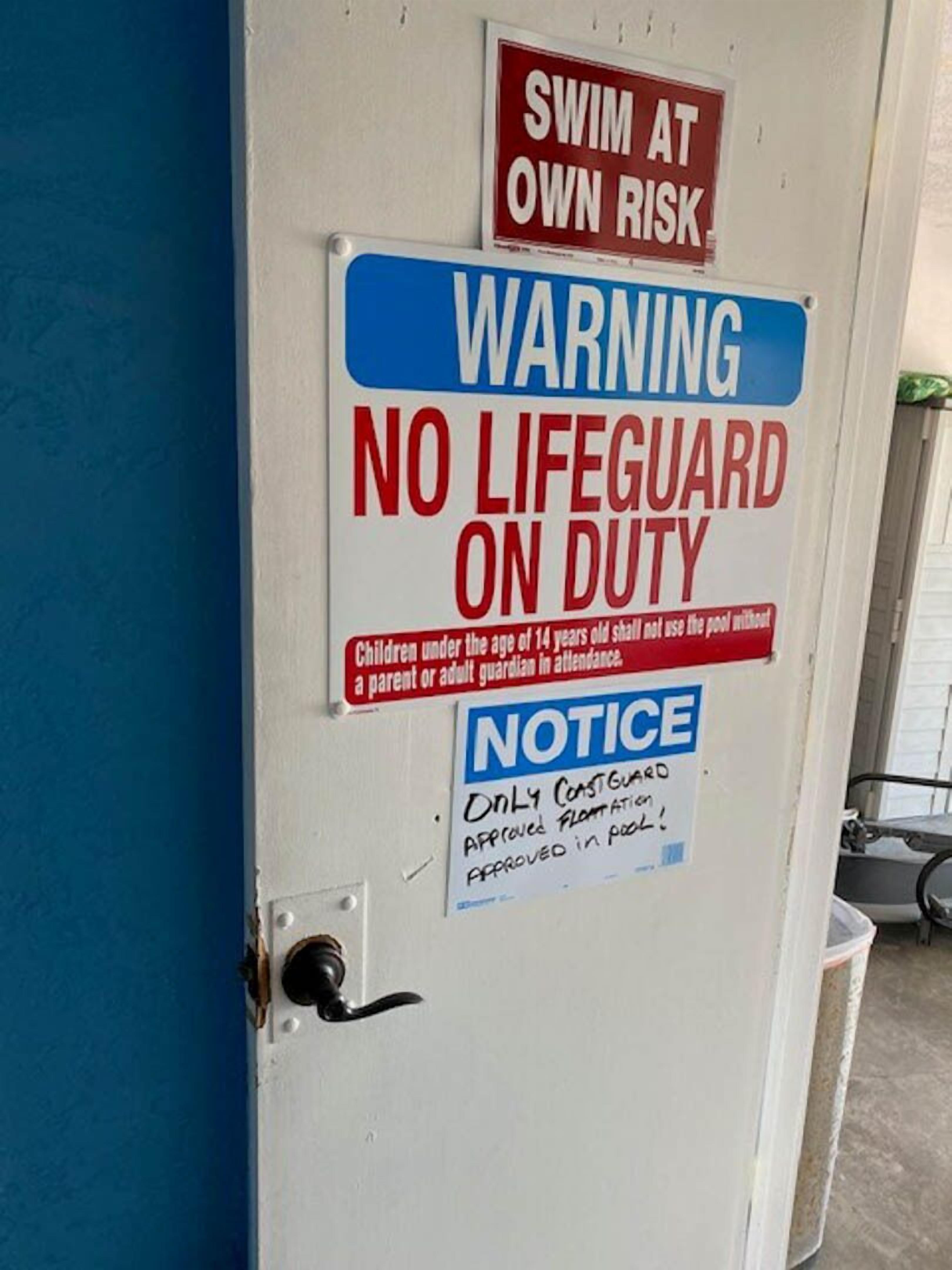 A door with multiple signs including 'SWIM AT OWN RISK', 'WARNING NO LIFEGUARD ON DUTY', and 'NOTICE Only Coastguard Approved Floatation Approved in Pool'.