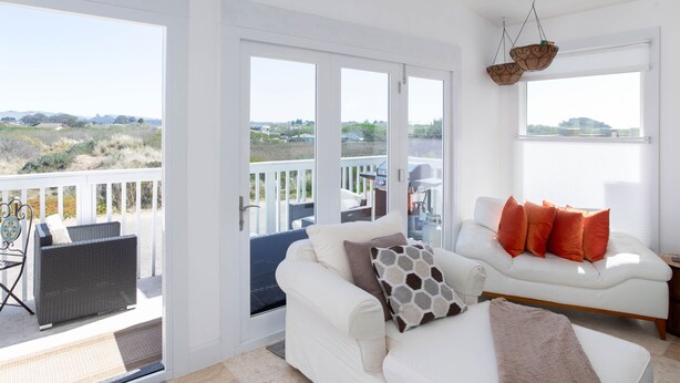A spacious living area with a white sofa, a wicker chair, and a balcony with a view of the countryside.