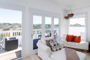 Un salón espacioso con un sofá blanco, una silla de mimbre y un balcón con vistas al campo.