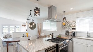A modern kitchen with a granite countertop, stainless steel appliances, and a dining area with white chairs and a table.