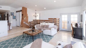 A spacious living room with a white sofa, a wooden accent wall, a chandelier, and a view through a glass door.