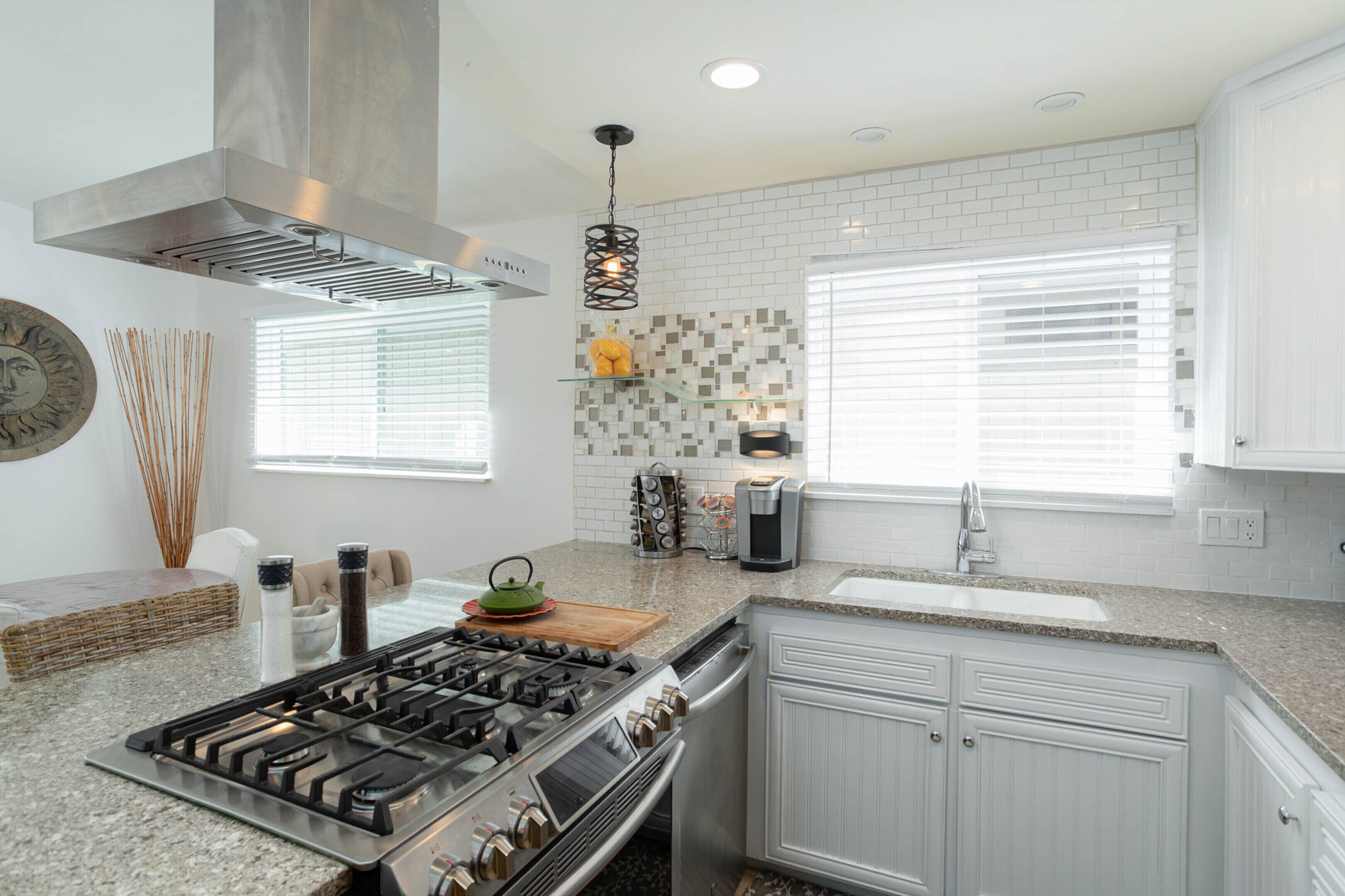 A modern kitchen with a gas stove, stainless steel range hood, white cabinets, and a granite countertop.