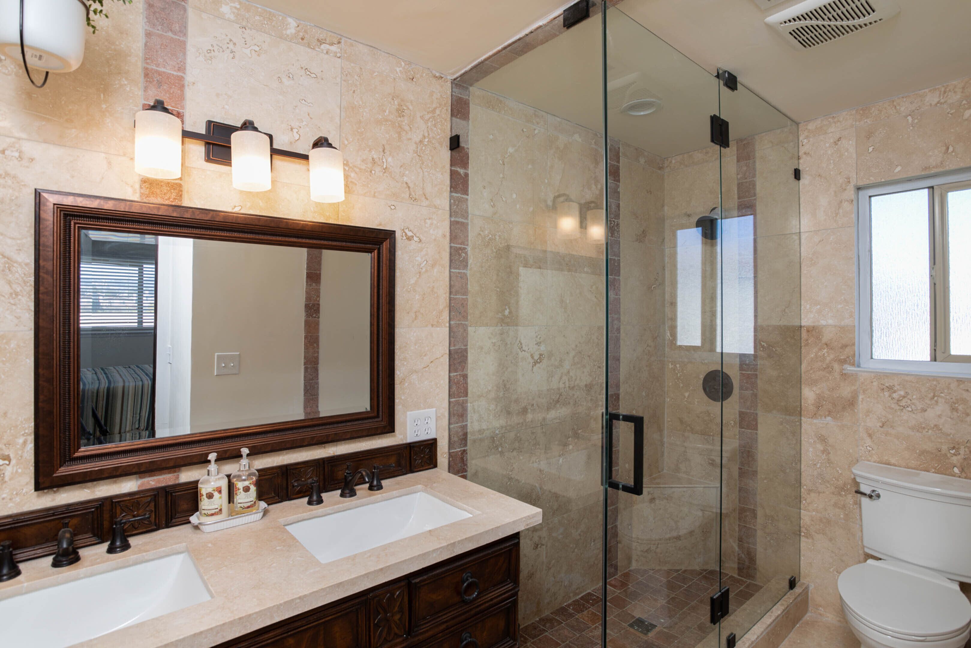 Une salle de bain avec deux lavabos, un grand miroir et une douche à parois de verre.
