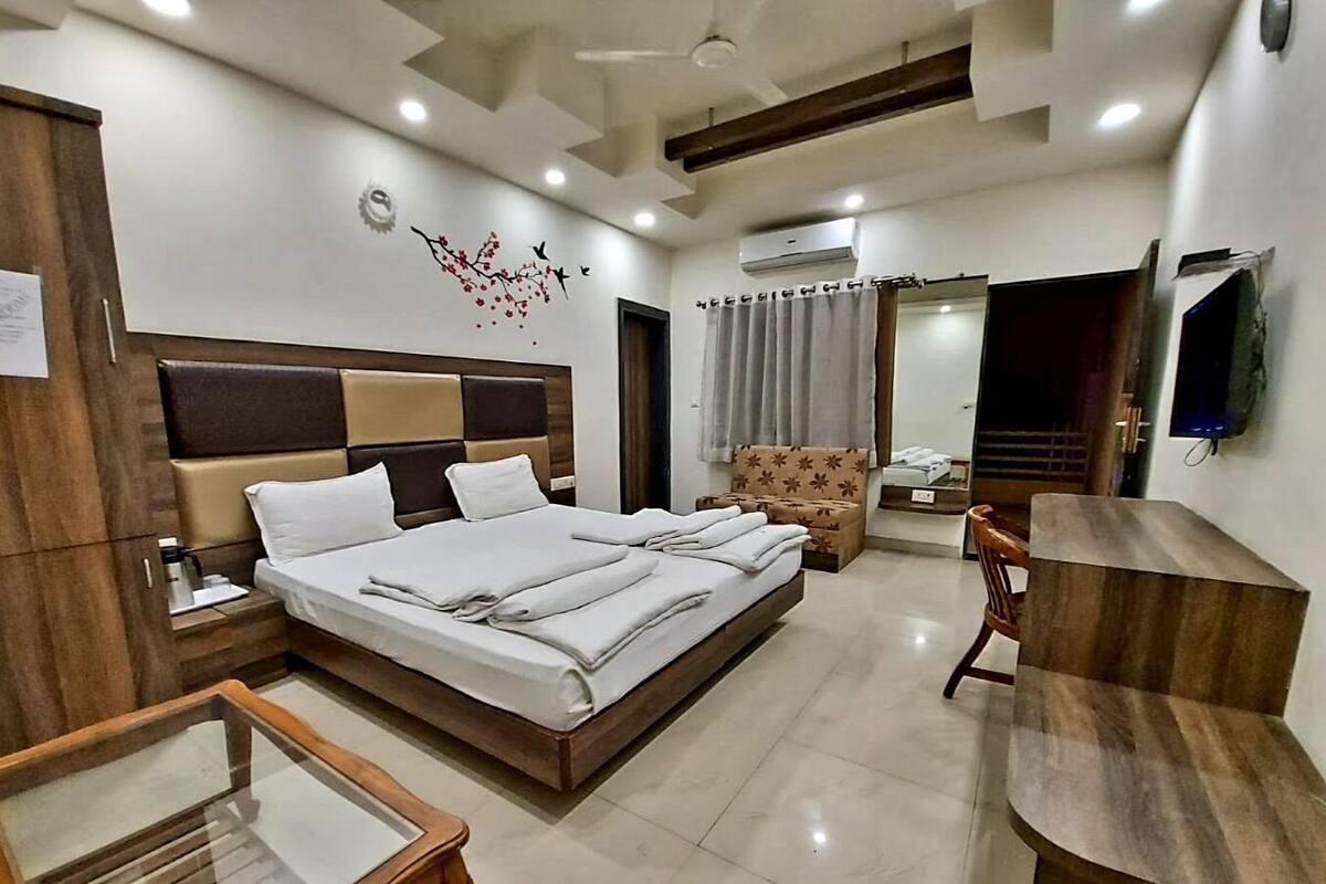 Habitación de hotel con una cama grande, cabecero de madera, escritorio, silla, armario, espejo y ventilador de techo.