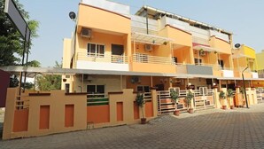 Un edificio residencial de varios pisos con balcones, plantas en macetas y un área de entrada pavimentada.