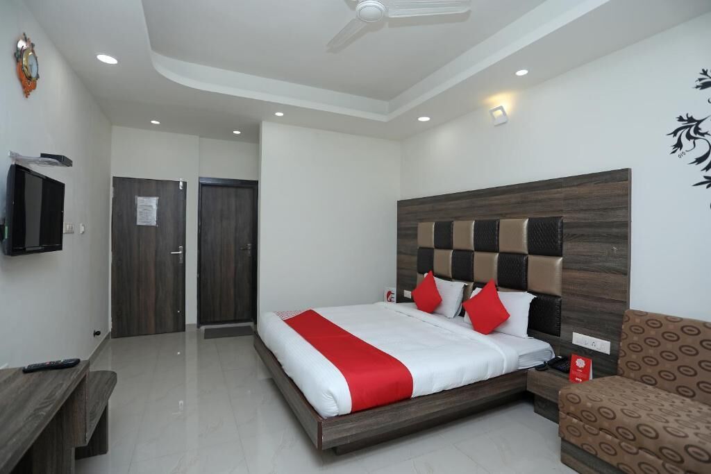 A modern hotel room with a large bed, a TV, a desk, and a patterned armchair.