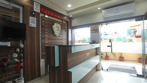 Zona de recepción de un hotel con un mostrador de madera, un reloj de pared y un televisor.