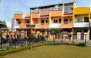 Stylish residential building with a flat roof and balcony, set amidst a well-manicured lawn and trees.