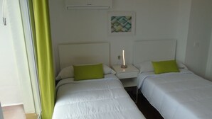 Ein Hotelzimmer mit zwei Einzelbetten, einem Nachttisch mit Lampe, einer Wand-Klimaanlage und einem gerahmten Kunstwerk über den Betten.