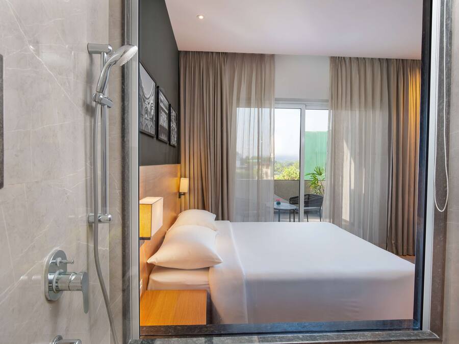 A modern hotel room with a large bed, a shower, and a balcony with a view.
