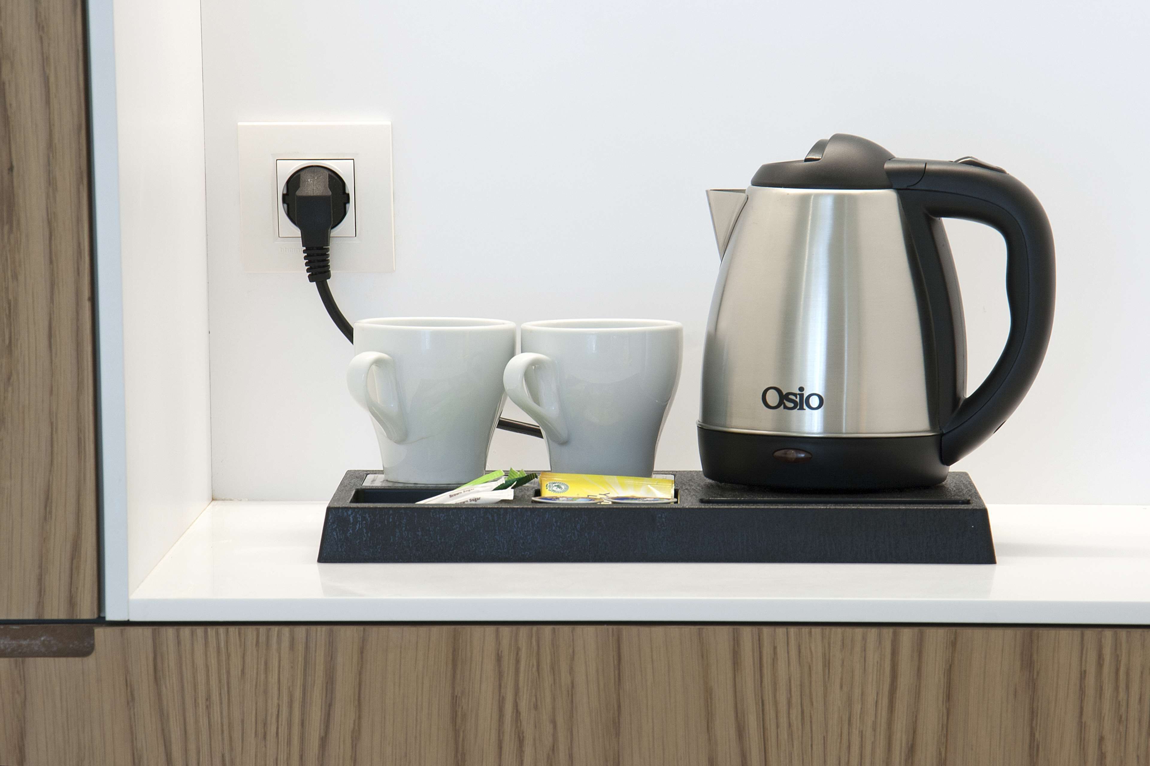 A kitchen counter with a kettle, two cups, and a power outlet.