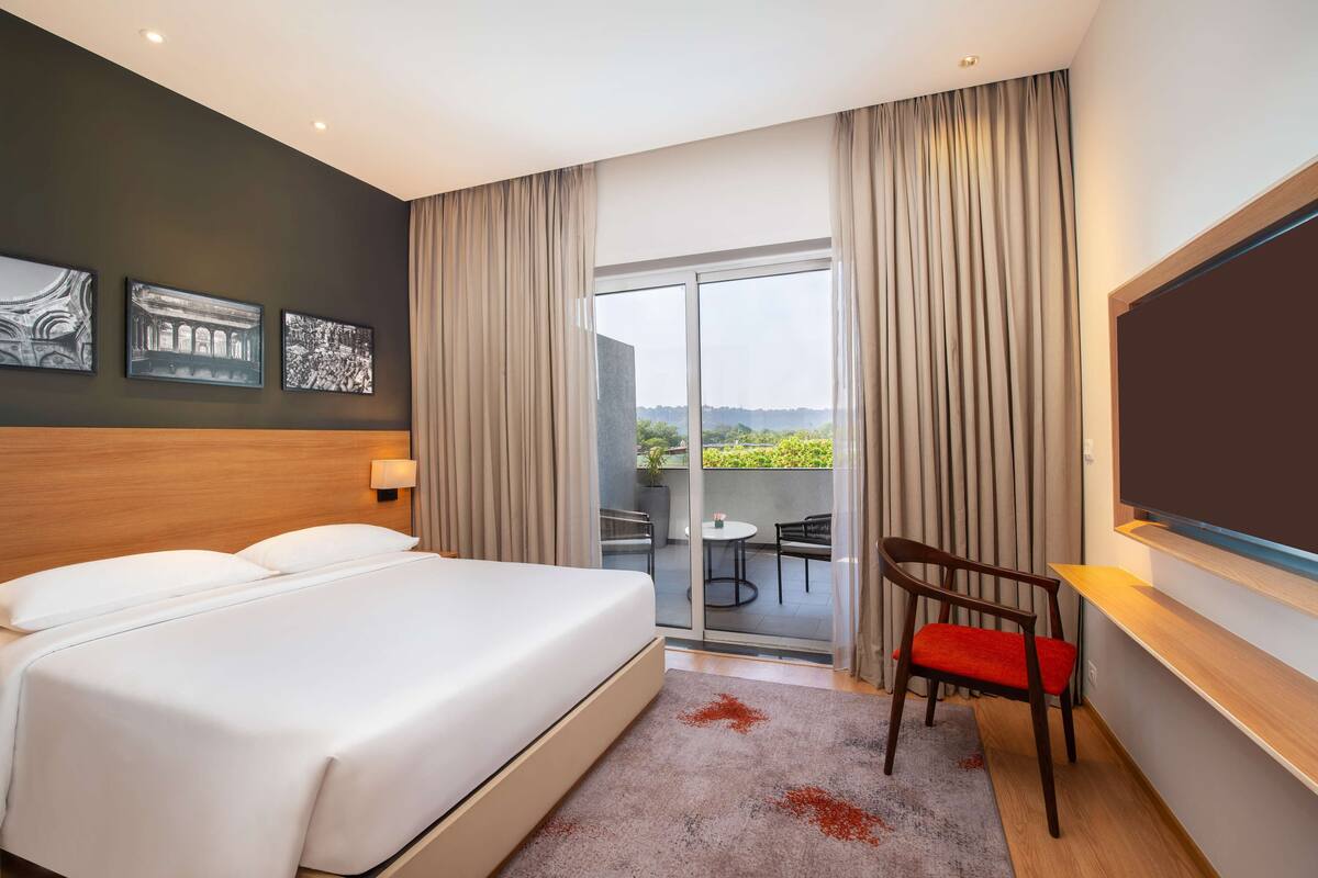 A hotel room with a large bed, a TV, a desk, and a balcony with a view.