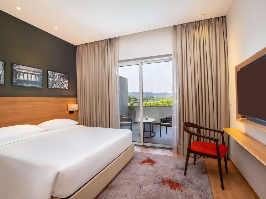 Habitación de hotel con una cama grande, televisión, escritorio y balcón con vistas.