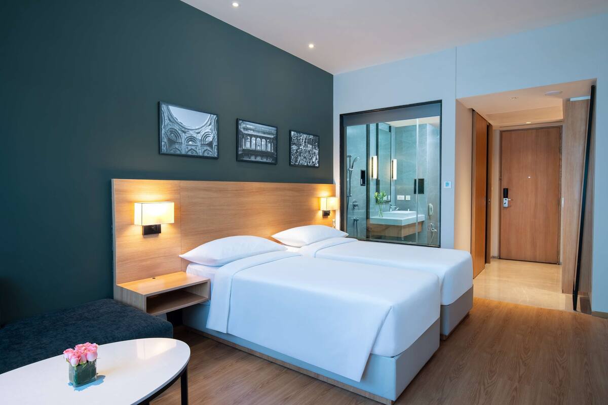 A hotel room with a double bed, bedside tables, a small table with a vase of flowers, and a large mirror.
