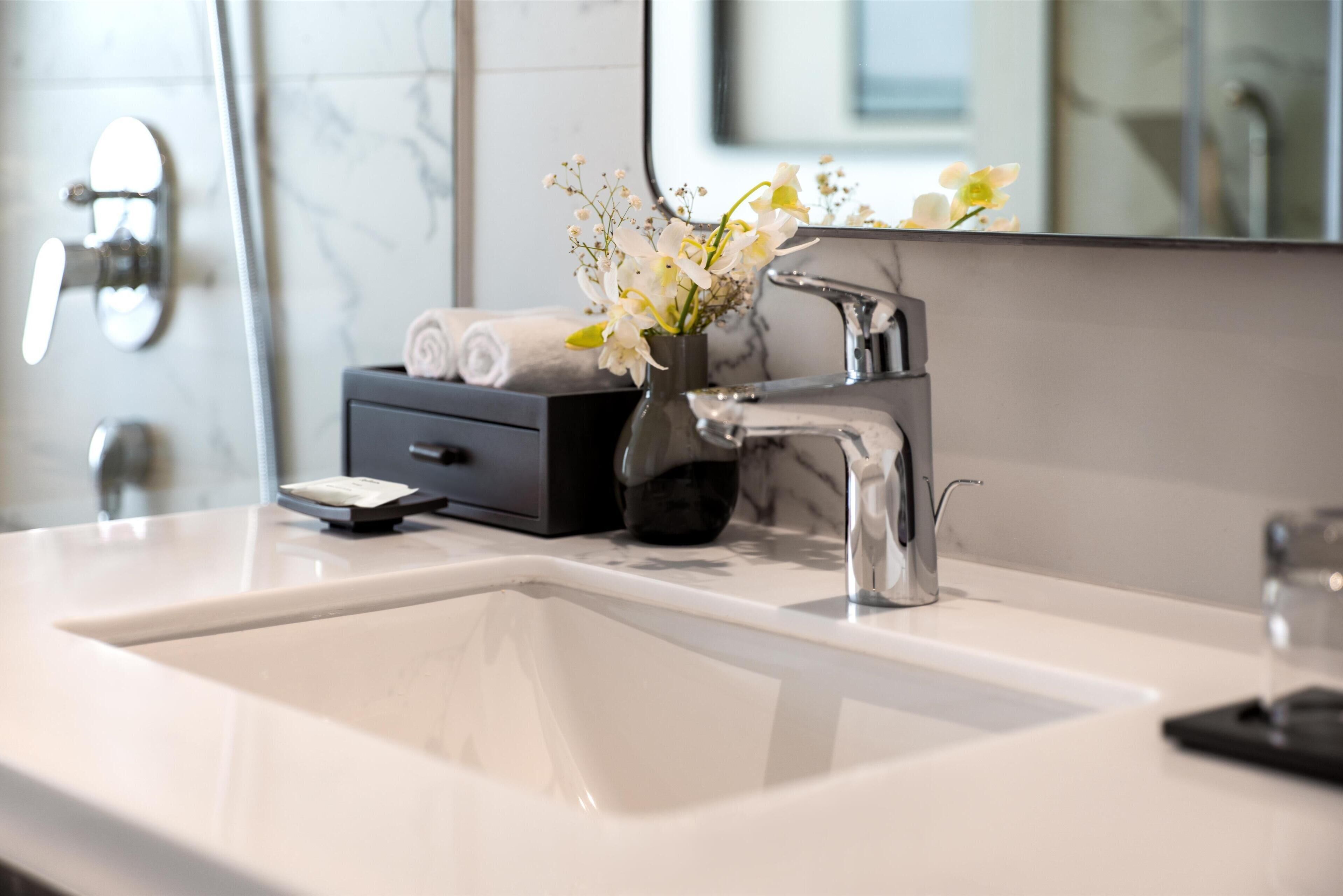 A modern bathroom with a white sink, chrome faucet, and a vase with flowers.