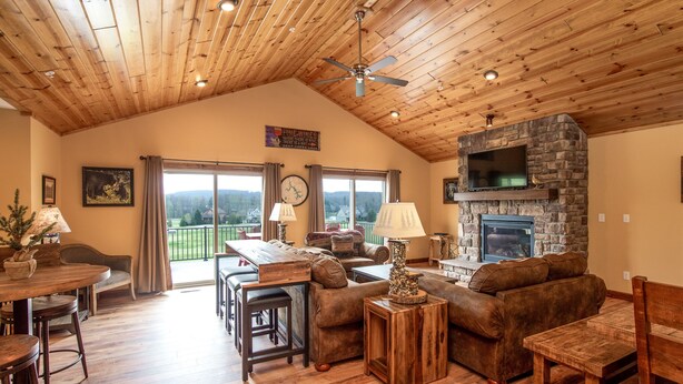 A spacious living room with a high ceiling, wooden floors, a stone fireplace, and a large window overlooking a scenic view.