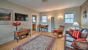 A living room with a wooden floor, a brown leather sofa, a rocking chair, a dining table with chairs, a wooden sideboard, and a large rug. - Well-Equipped Cody Cottage: 2 Mi to Cody Rodeo! (Cody)