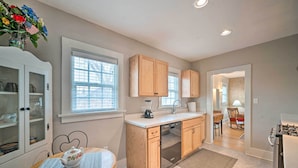 A modern kitchen with wooden cabinets, a dishwasher, and a dining area with a table and chairs. - Well-Equipped Cody Cottage: 2 Mi to Cody Rodeo! (Cody)
