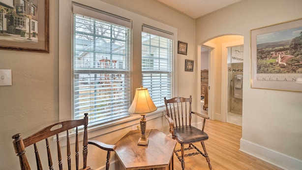 A dining area with a wooden table, two chairs, a table lamp, and large windows with blinds. - Well-Equipped Cody Cottage: 2 Mi to Cody Rodeo! (Cody)