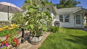 A garden with a variety of flowers and plants, a wooden planter, and a house with a white exterior and a gray roof. - Well-Equipped Cody Cottage: 2 Mi to Cody Rodeo! (Cody)