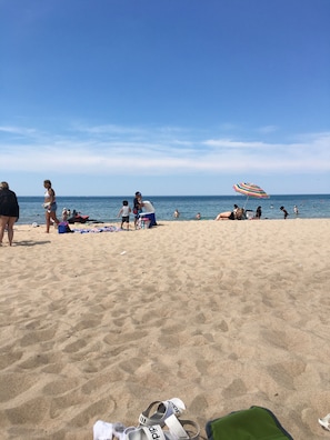 Une plage de sable où se trouvent des gens, un parasol rayé et un bateau sur l’eau.