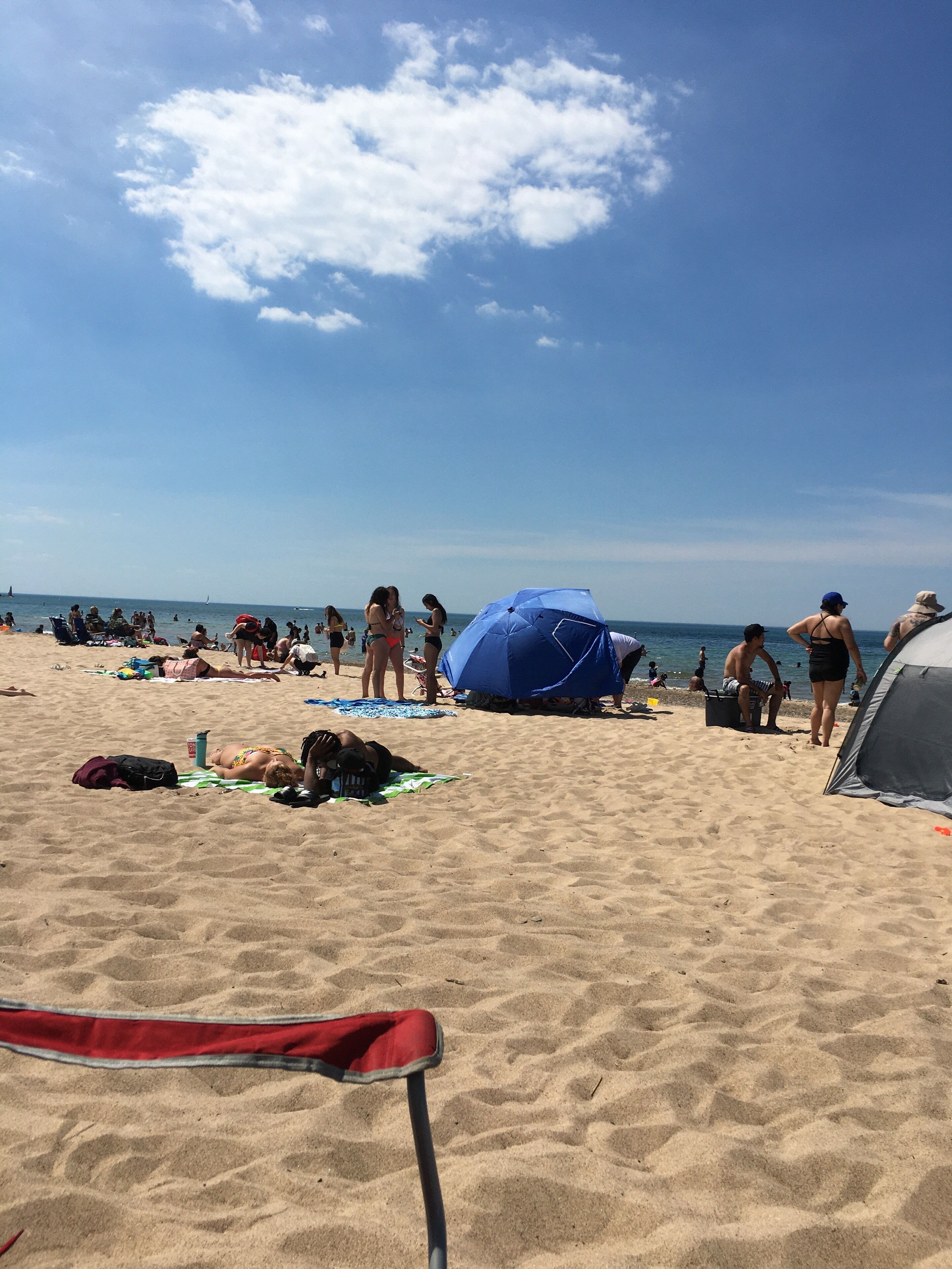 A beach scene with people sunbathing, a tent, and a blue umbrella.