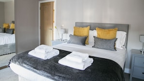 Une chambre d’hôtel moderne avec un grand lit, deux tables de chevet, une petite table et un miroir.