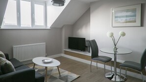 Un salon moderne avec un téléviseur, deux fauteuils, une petite table et un tableau accroché au mur.